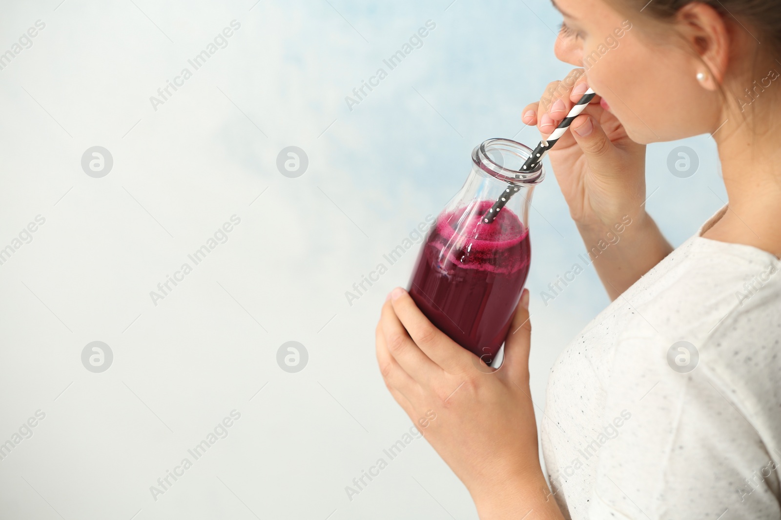 Photo of Woman holding bottle of beet smoothie on light background with space for text, closeup