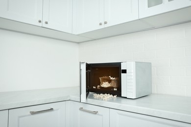 Open microwave oven with fresh popcorn on countertop in kitchen