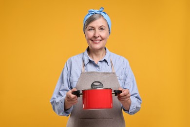 Happy housewife with pot on orange background