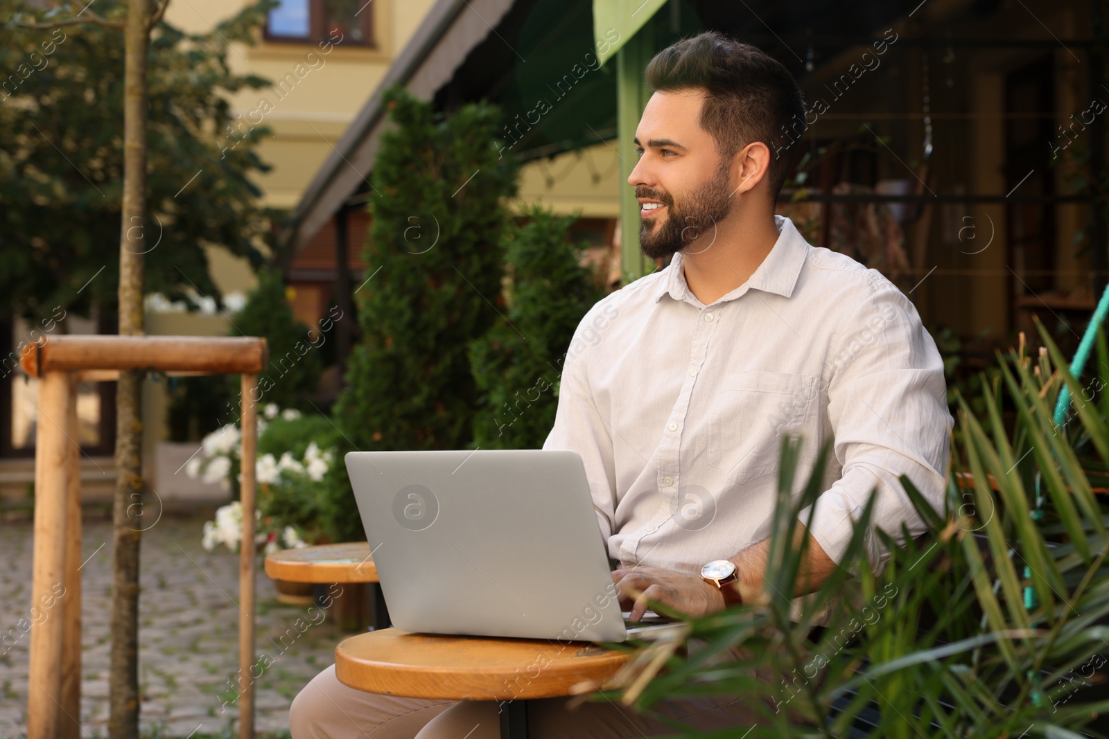 Photo of Handsome young man working on laptop at table in outdoor cafe