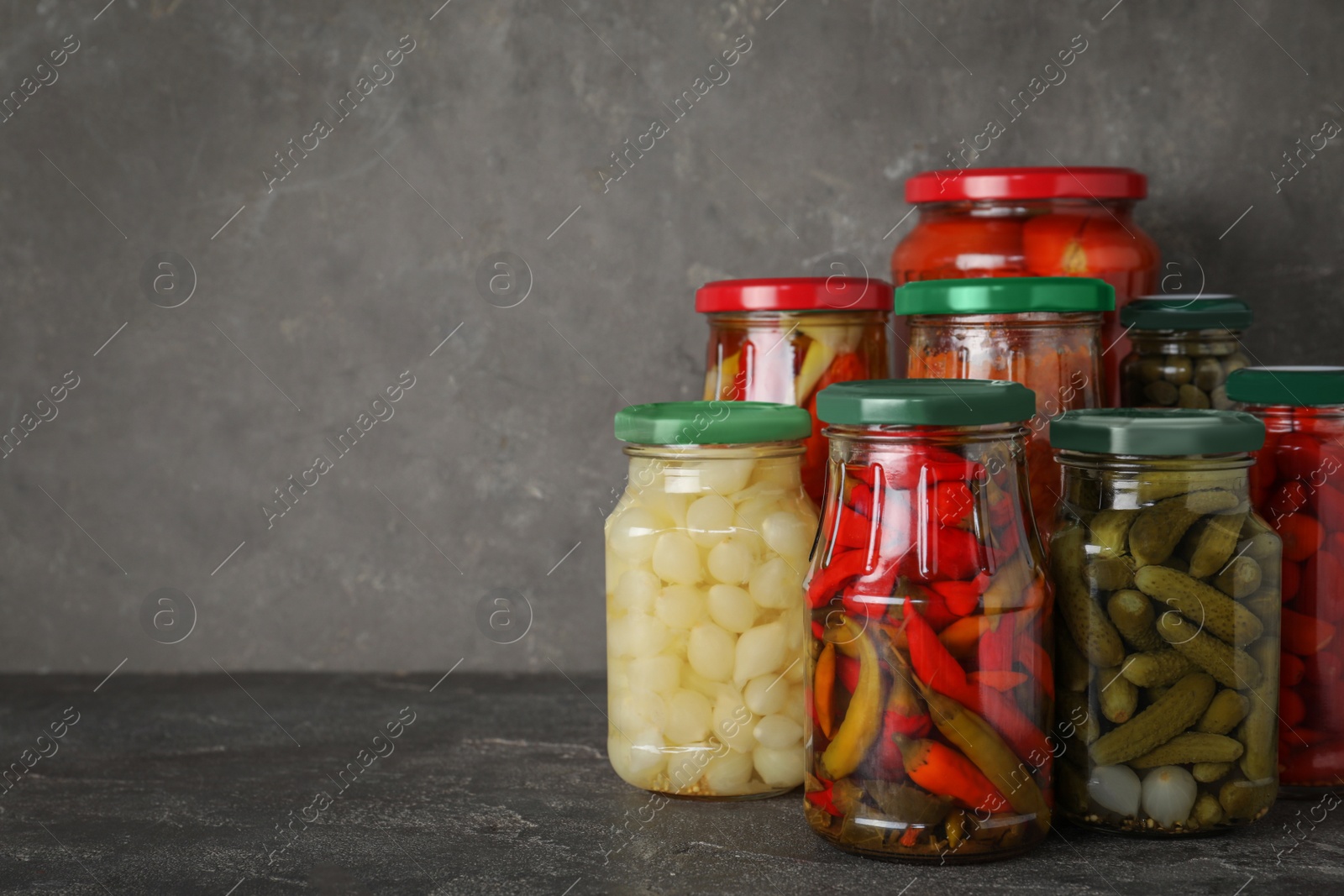 Photo of Jars of tasty pickled vegetables on grey table. Space for text