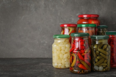 Photo of Jars of tasty pickled vegetables on grey table. Space for text