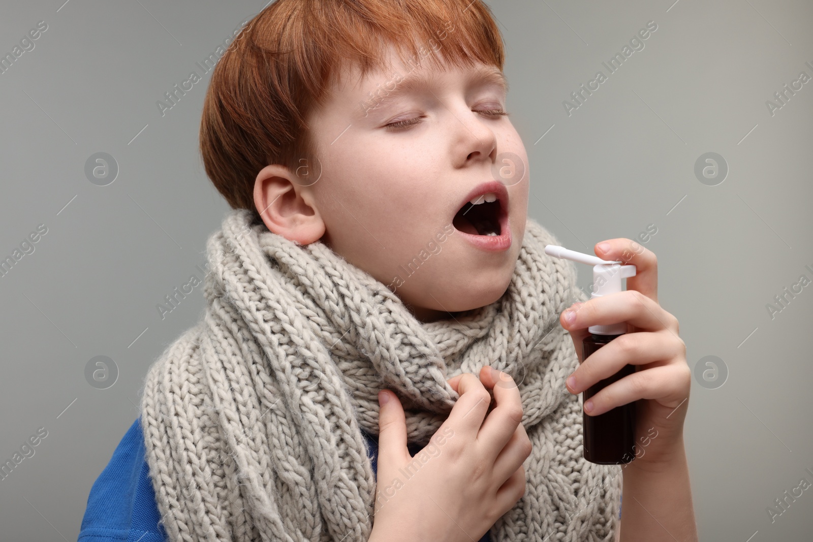 Photo of Little boy with scarf using throat spray on grey background