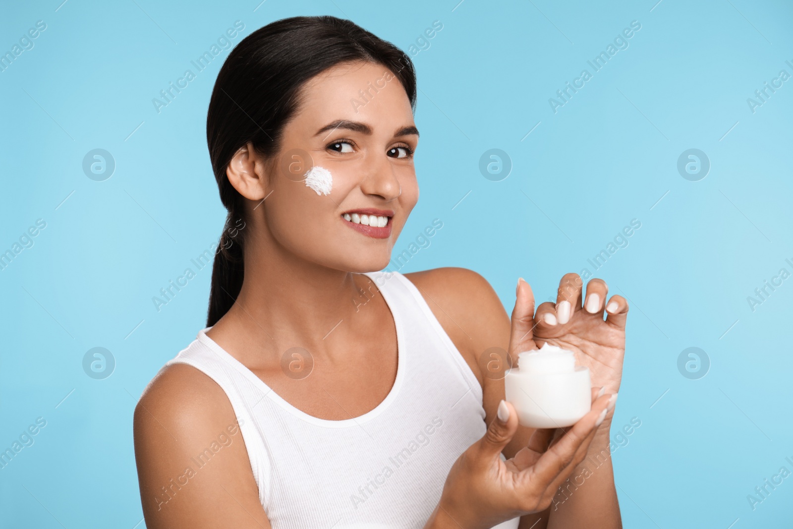 Photo of Young woman applying facial cream on light blue background