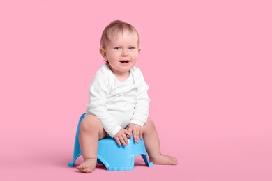 Little child sitting on baby potty against pink background