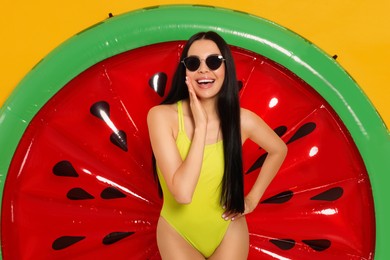 Young woman with stylish sunglasses near inflatable mattress against orange background