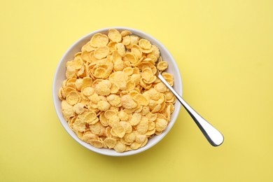 Photo of Breakfast cereal. Tasty corn flakes in bowl and spoon on yellow table, top view