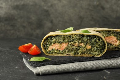 Photo of Pieces of delicious strudel with salmon and spinach served on dark textured table, closeup