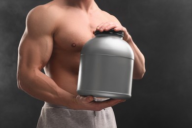 Photo of Young man with muscular body holding jar of protein powder on dark grey background, closeup