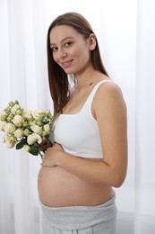Photo of Beautiful pregnant woman with bouquet of roses near window indoors