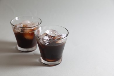 Photo of Refreshing iced coffee in glasses on grey background. Space for text