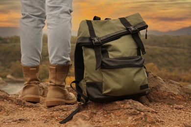 Photo of Traveler with backpack on steep cliff near mountain river, closeup. Autumn vacation