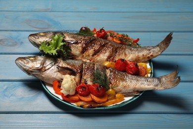 Plate with delicious baked sea bass fish and vegetables on light blue table