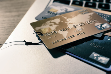 Photo of Fishing hook with credit cards and laptop on table, closeup. Cyber crime