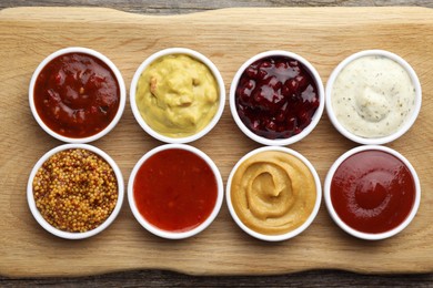 Different tasty sauces in bowls on wooden board, top view