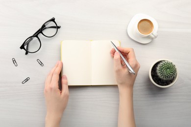 Photo of Woman writing in notebook at light wooden table, top view