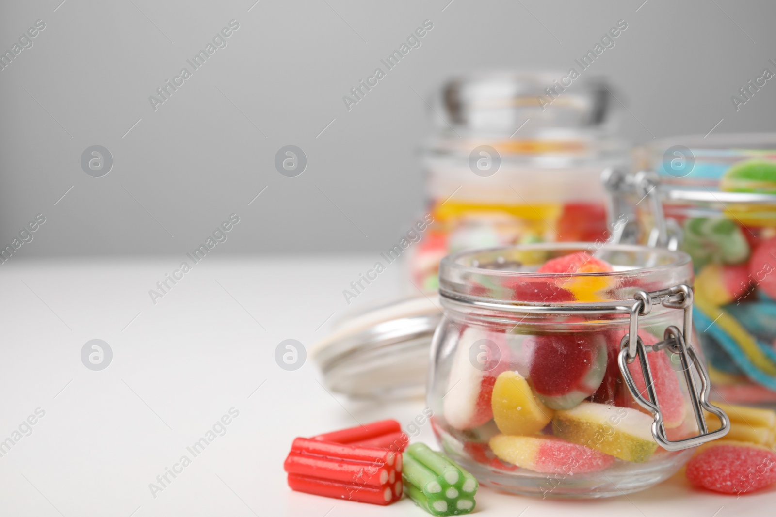 Photo of Tasty jelly candies in jars on white table, space for text