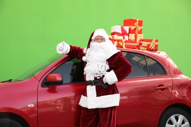 Photo of Authentic Santa Claus near car with presents on roof against green background