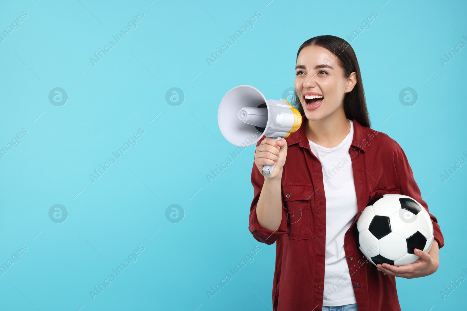 Photo of Happy fan with soccer ball using megaphone on light blue background, space for text