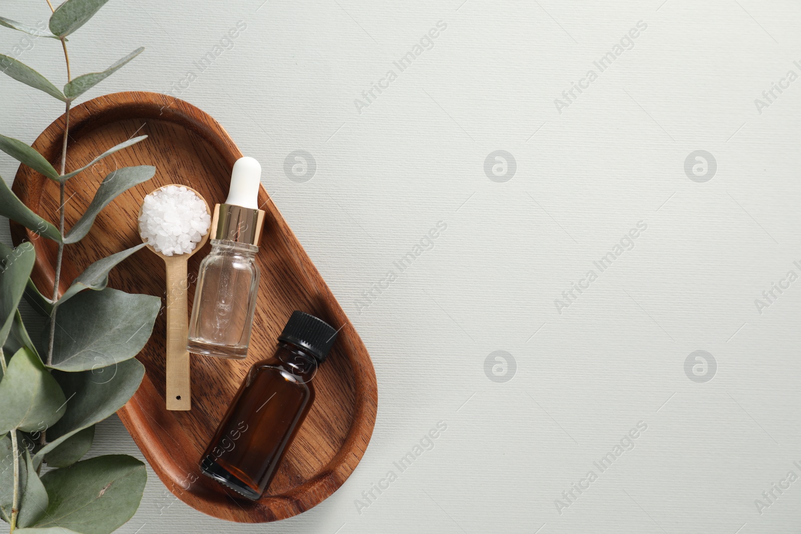 Photo of Aromatherapy products. Bottles of essential oil, sea salt and eucalyptus leaves on grey background, flat lay. Space for text