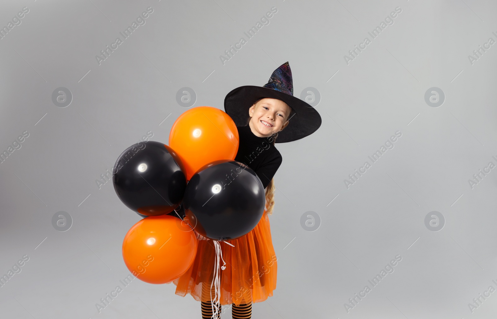 Photo of Cute little girl with balloons wearing Halloween costume on grey background, space for text