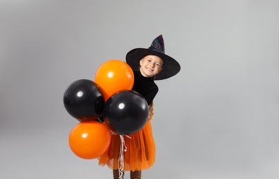 Cute little girl with balloons wearing Halloween costume on grey background, space for text