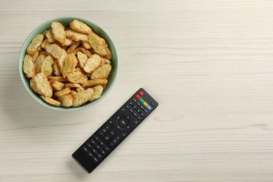 Photo of Modern tv remote control and rusks on white wooden table, flat lay. Space for text