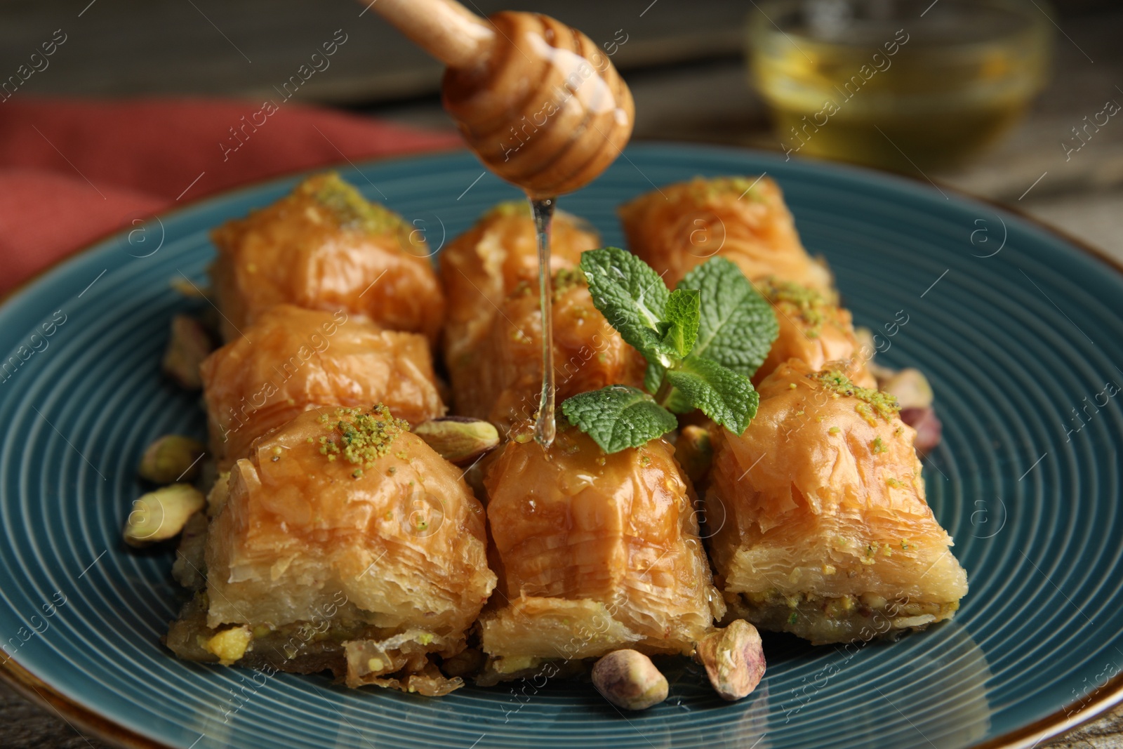 Photo of Pouring honey onto delicious baklava with pistachios and mint on table, closeup