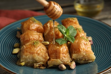 Photo of Pouring honey onto delicious baklava with pistachios and mint on table, closeup