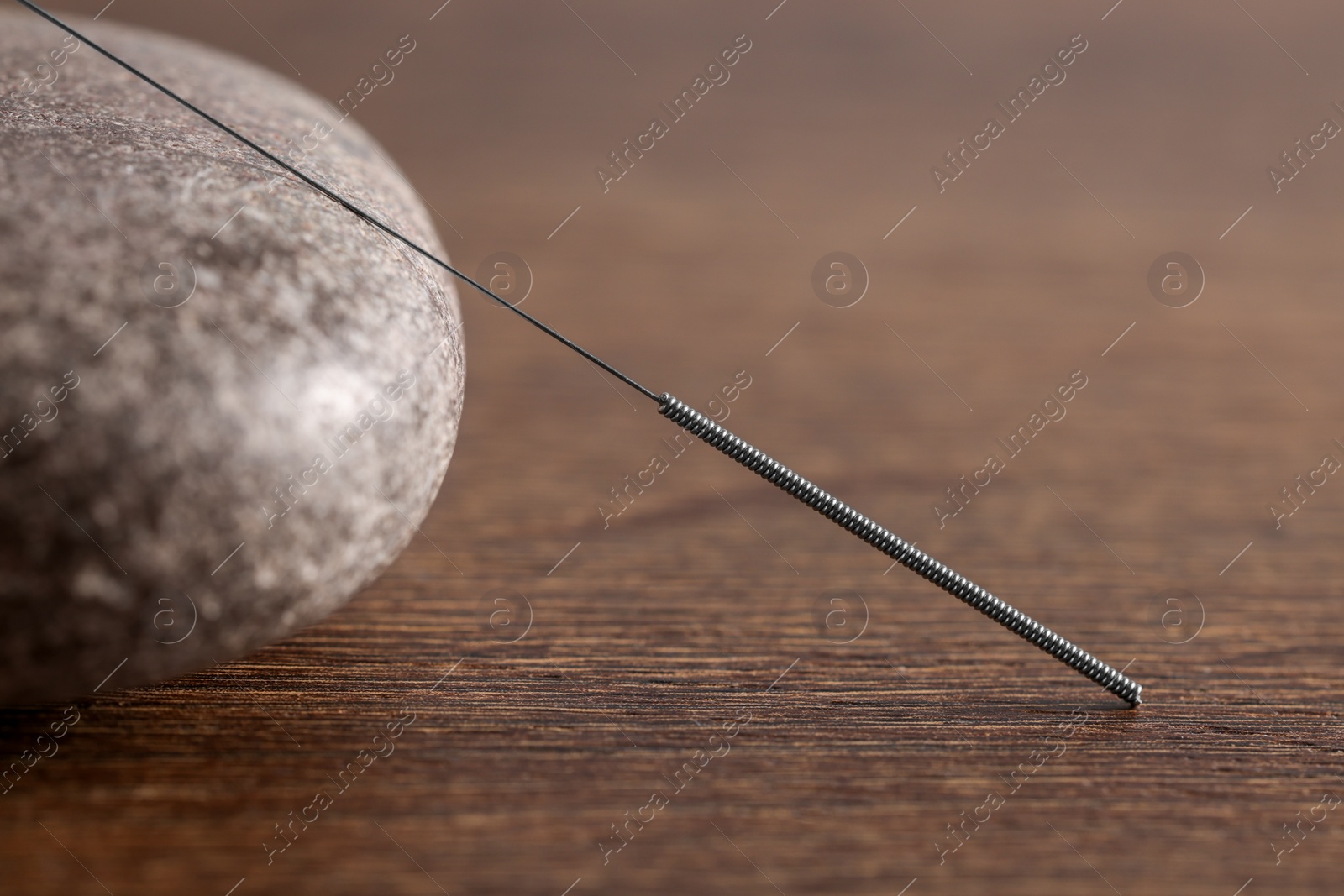 Photo of Acupuncture needle and spa stone on wooden table, closeup