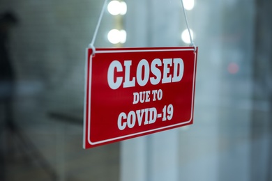 Photo of Red sign with text Closed Due To Covid-19 hanging on glass door, closeup. Coronavirus quarantine