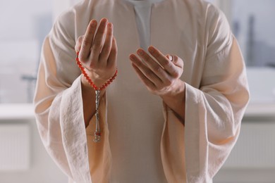 Photo of Muslim man with misbaha praying near window indoors, closeup