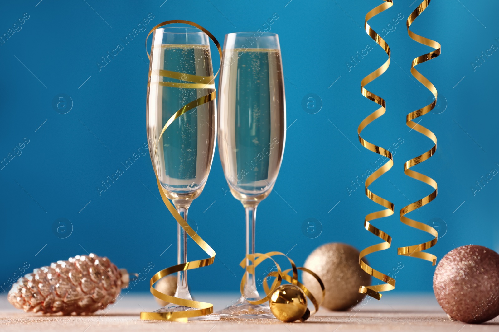 Photo of Glasses of champagne with serpentine streamers and Christmas ornaments on table against blue background