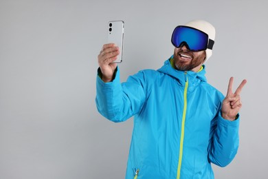 Photo of Winter sports. Happy man in ski and goggles suit taking selfie on gray background, space for text