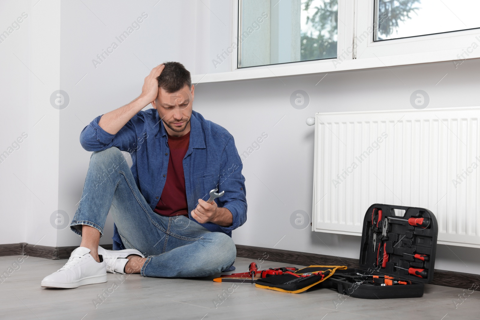 Photo of Man holding wrench near box with tools indoors