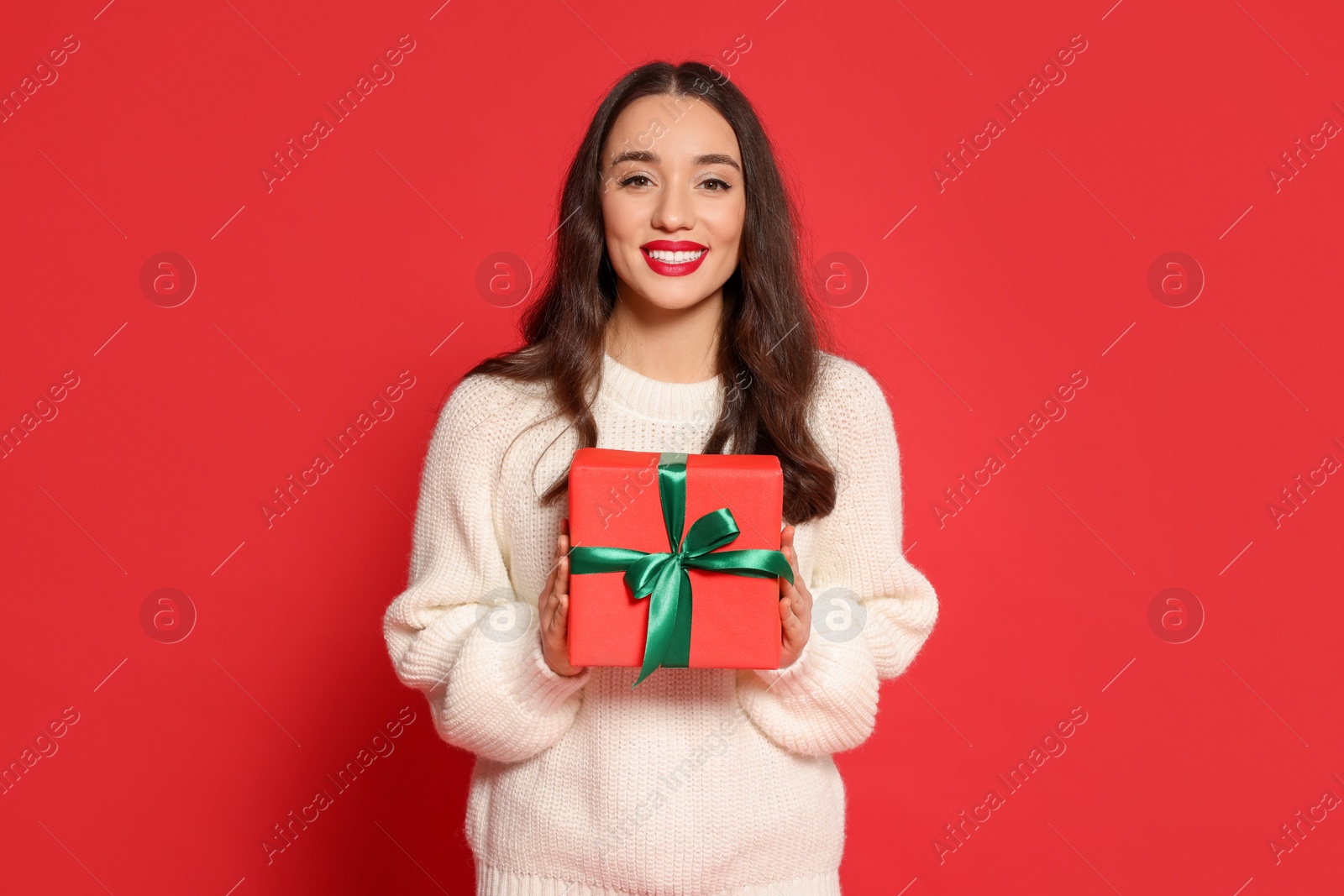 Photo of Beautiful young woman with Christmas gift on red background