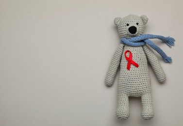 Photo of Cute knitted toy bear with red ribbon on beige background, top view and space for text. AIDS disease awareness
