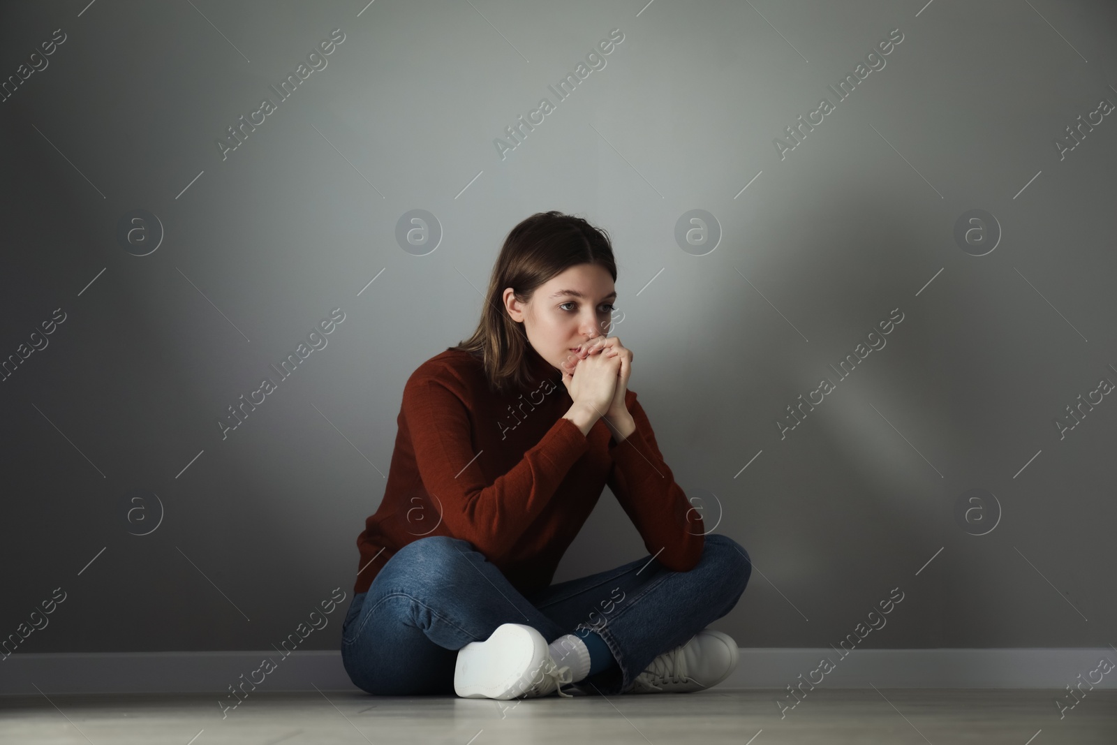 Photo of Sad young woman sitting on floor near grey wall indoors