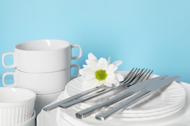 Set of clean dishes and cutlery against light blue background, closeup