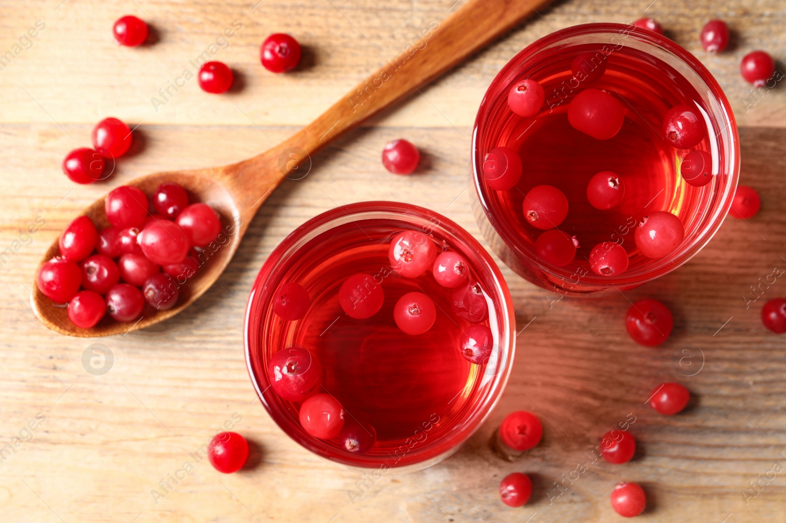 Photo of Tasty cranberry juice in glasses and fresh berries on wooden table, flat lay