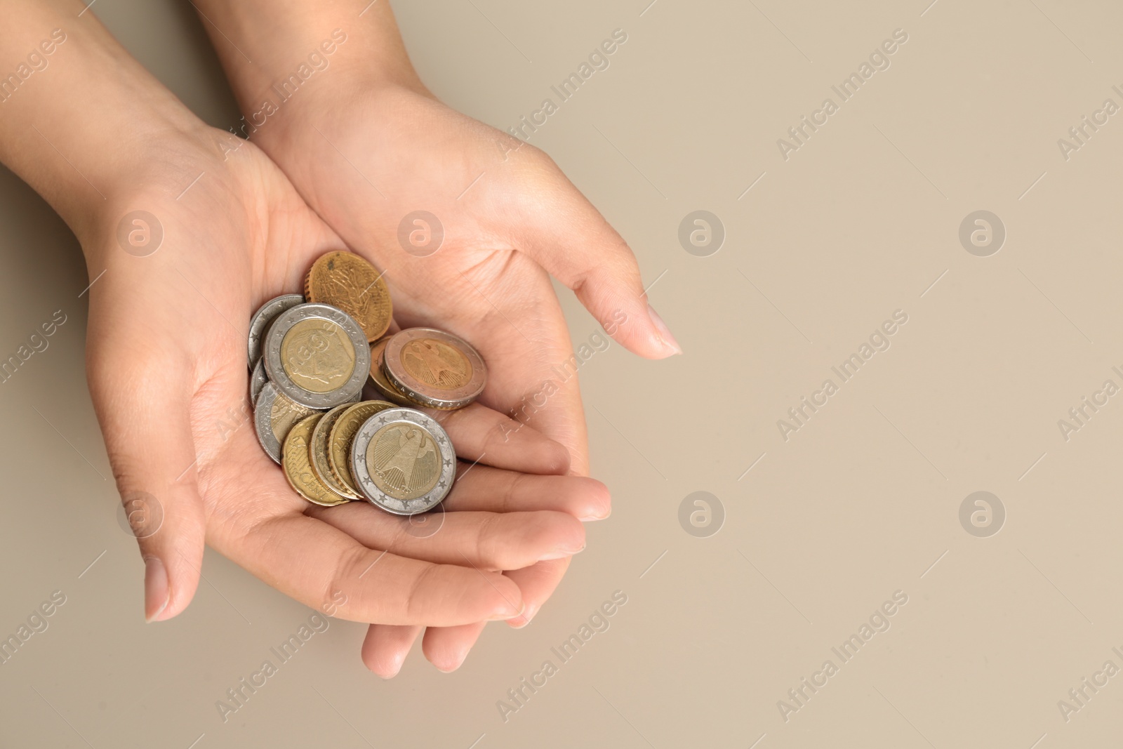 Photo of Young woman with handful of coins on beige background, above view. Space for text
