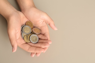 Photo of Young woman with handful of coins on beige background, above view. Space for text