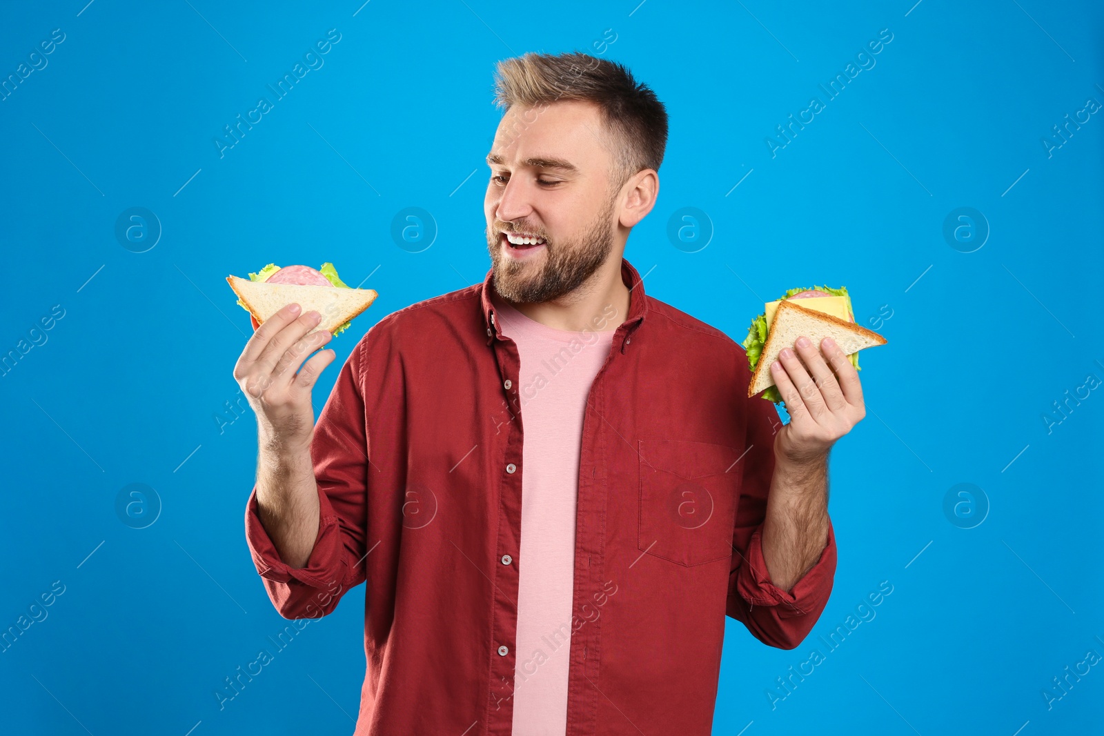 Photo of Young man with tasty sandwiches on light blue background