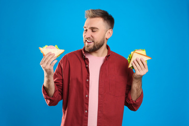 Young man with tasty sandwiches on light blue background