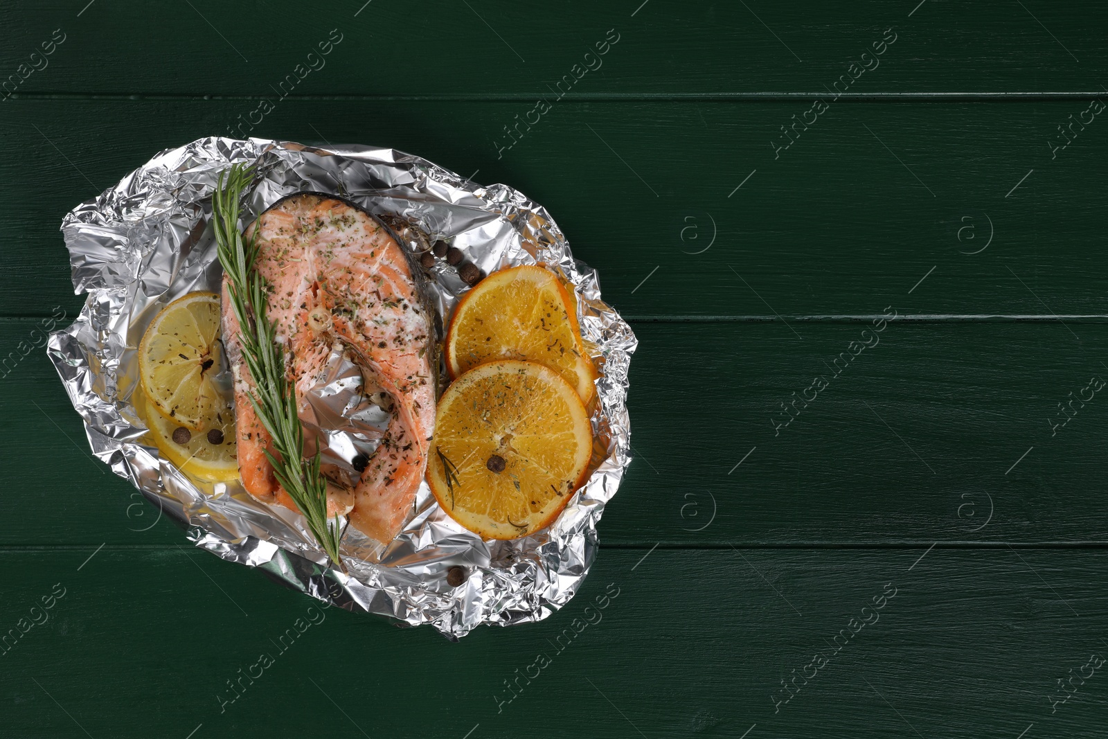 Photo of Tasty salmon baked in foil with citrus fruits and rosemary on green wooden table, top view. Space for text