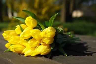 Photo of Bouquet of beautiful yellow tulips on wooden table outdoors