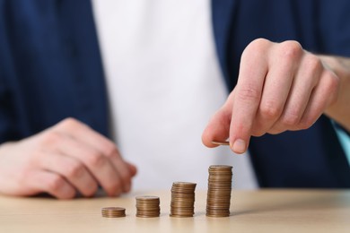 Photo of Financial savings. Man stacking coins at wooden table, closeup