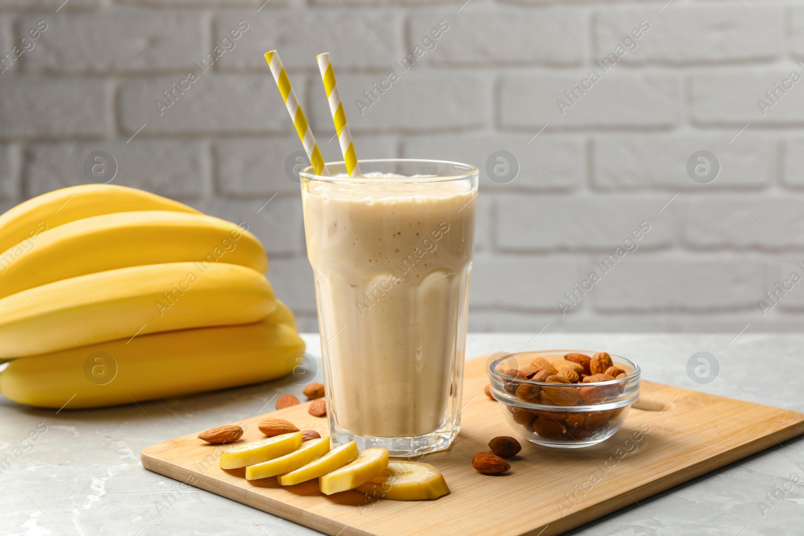 Photo of Banana smoothie in glass and nuts on light grey marble table against white brick wall