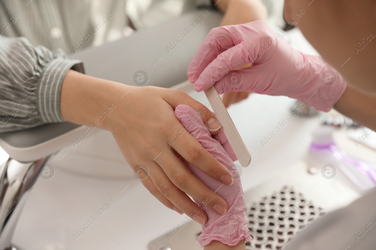 Photo of Professional manicurist filing client's nails in beauty salon, closeup