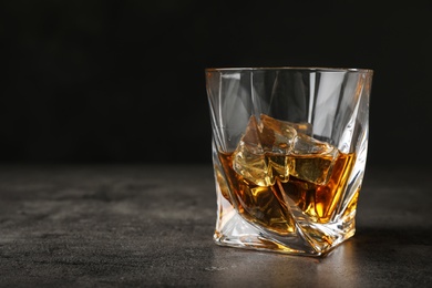 Photo of Golden whiskey in glass with ice cubes on table. Space for text